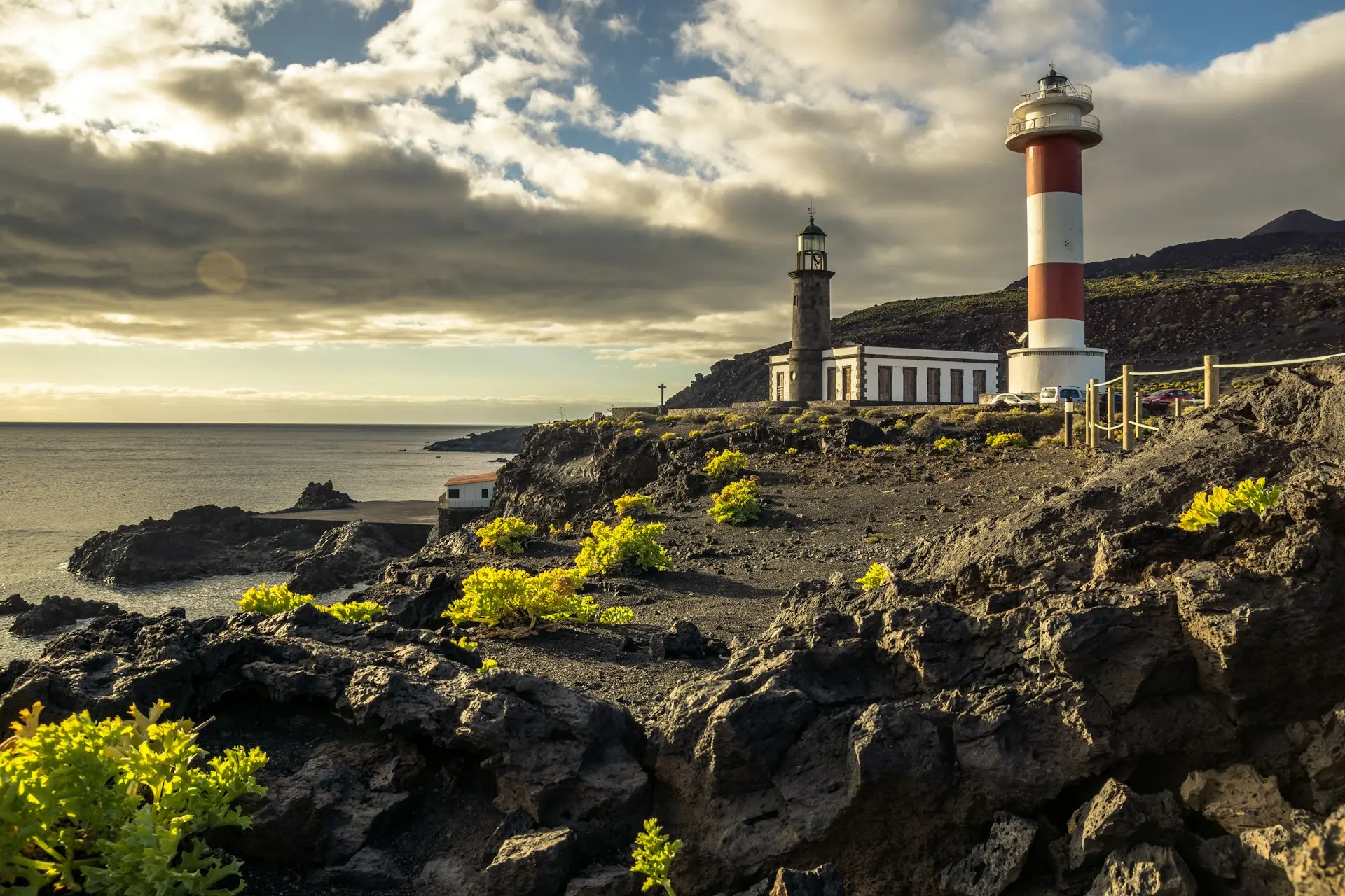 white and red lighthouse on rocky hill near sea under cloudy sky during daytime